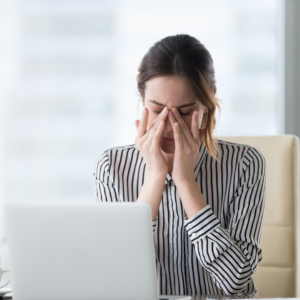 Woman sitting at a desk rubbing her eyes in fatigue, illustrating tiredness as a symptom of iron deficiency without anemia