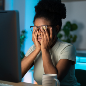Tired woman rubbing her eyes at computer showing iron deficiency symptoms like exhaustion