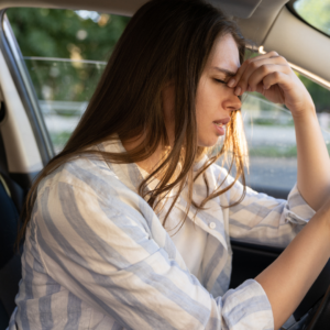 Tired woman pinching the bridge of her nose in a car, experiencing iron deficiency anemia symptoms