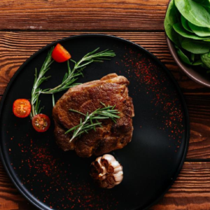 Cooked steak on a black plate with rosemary, garlic, and spinach, a top source of heme iron