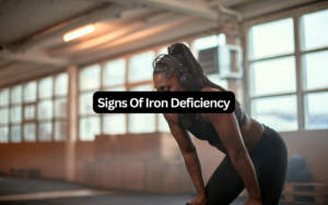 Signs of iron deficiency: exhausted woman in headphones resting hands on knees mid-workout in a gym