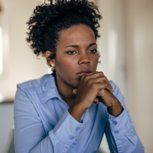 Woman with curly hair resting her chin on her hands, looking anxious, a possible sign of iron deficiency causing anxiety